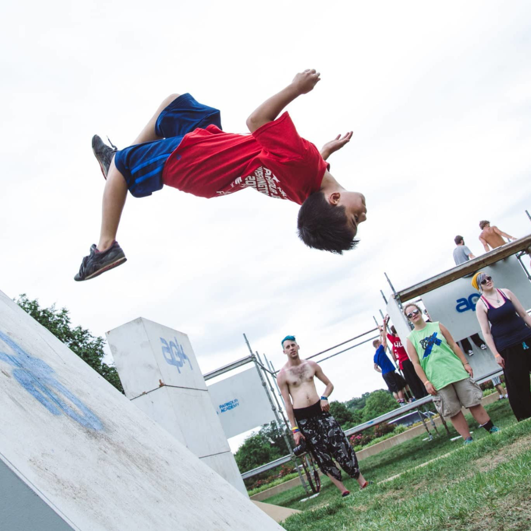 small boy performing parkour outdoors in front of a crowd