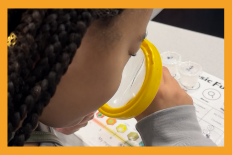 a young girl looks through a magnifying glass at a science experiment.