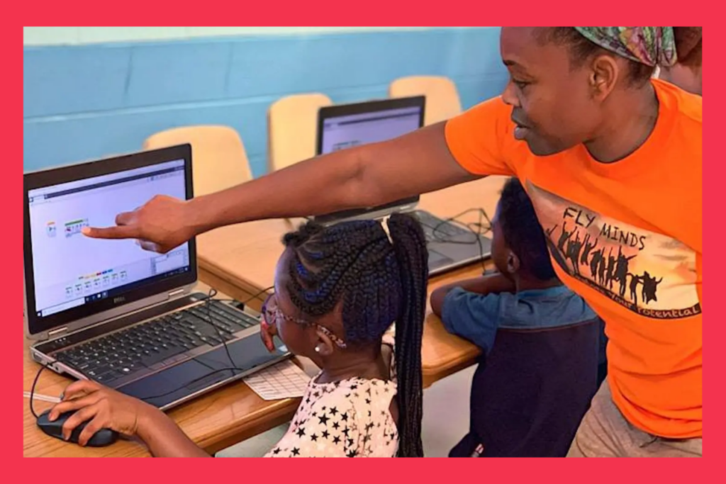 a mentor points at a computer screen aiding a young girl with work