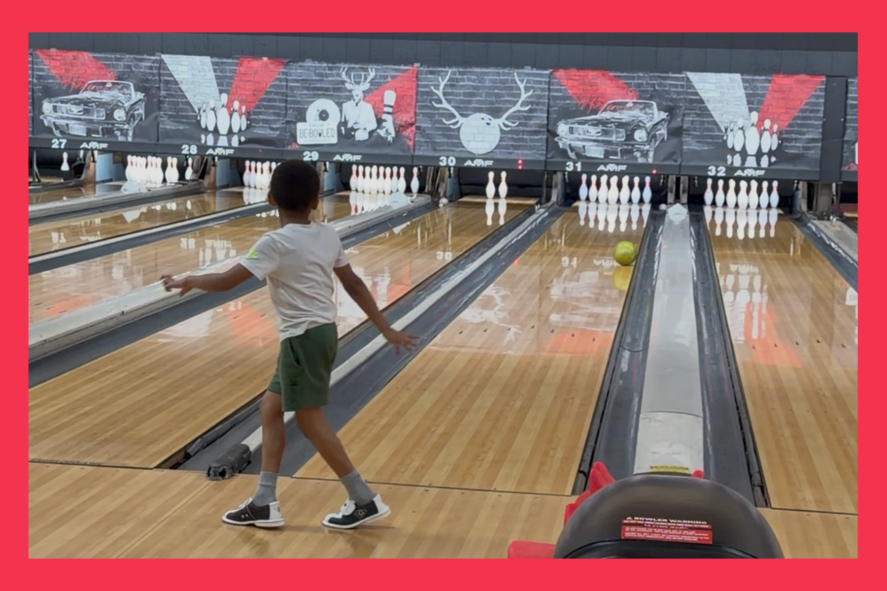 young boy watches bowling ball head down the lane towards the pins.