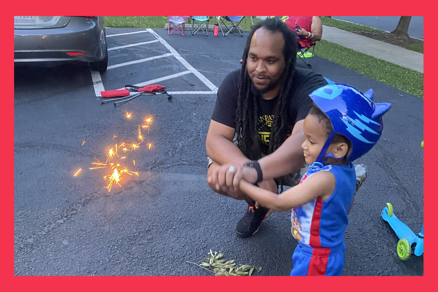 young boy holds a firework with his dad keeping a watchful eye in an open parking lot