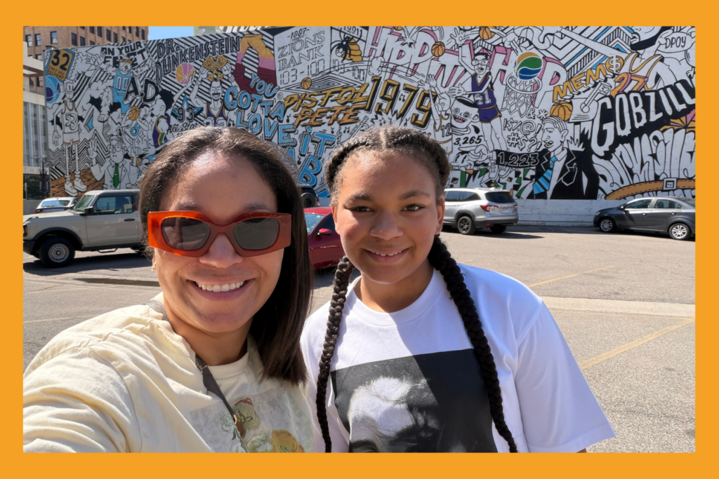 mom and daughter smile in front of a billboard.