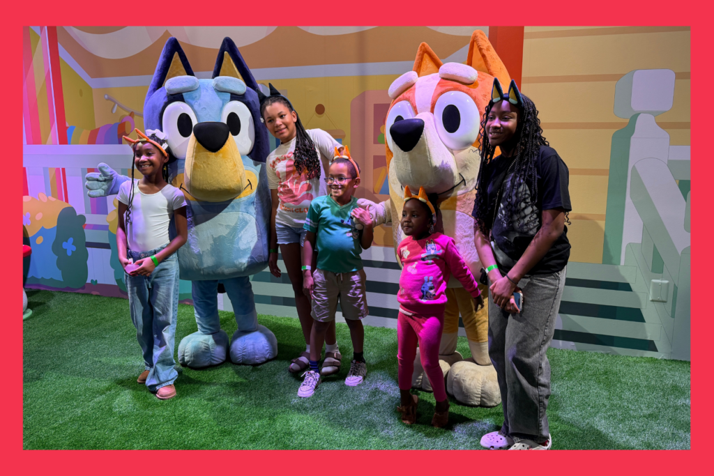 kids pose with Bluey characters on a green faux lawn.