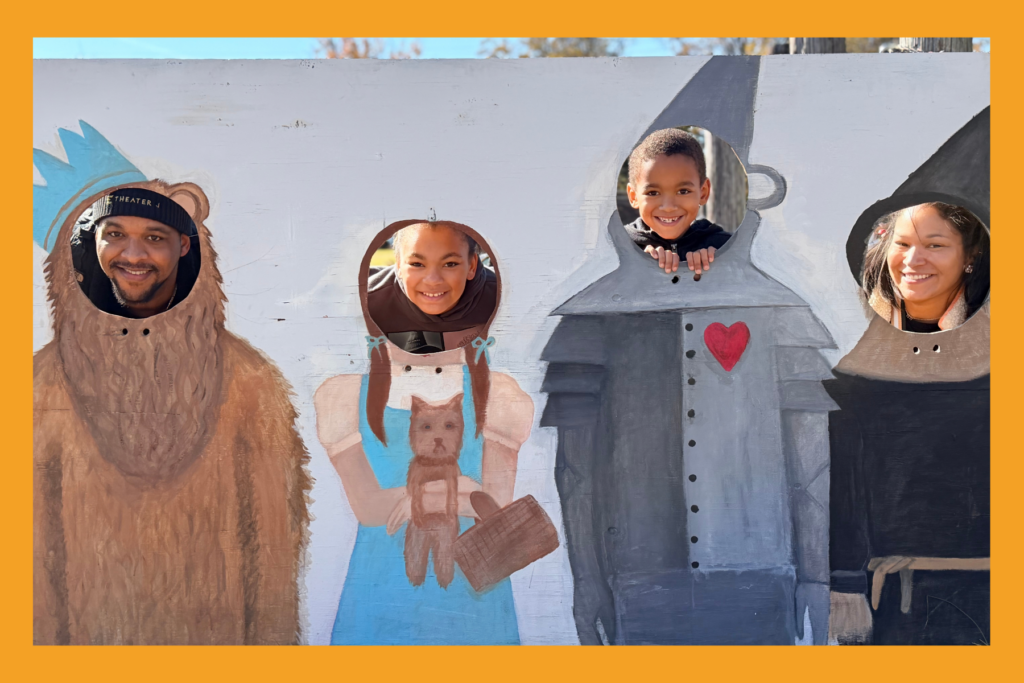 a family poses as wizard of oz characters behind a painted wooden board.