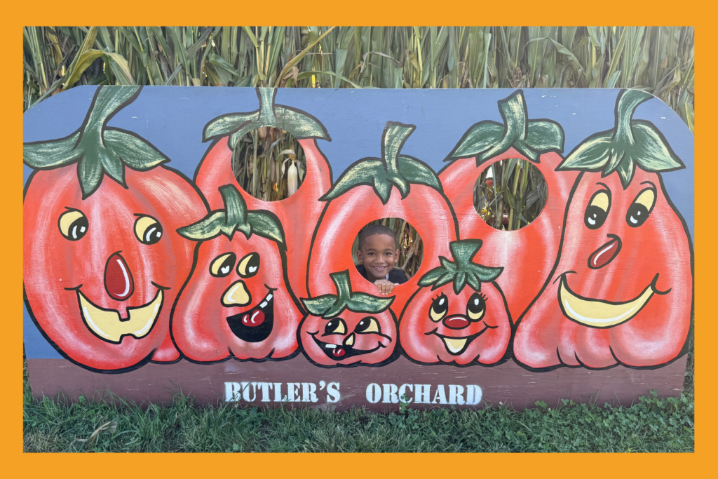 A boy poses behind a pumpkin painted wall at Butler's Orchard.