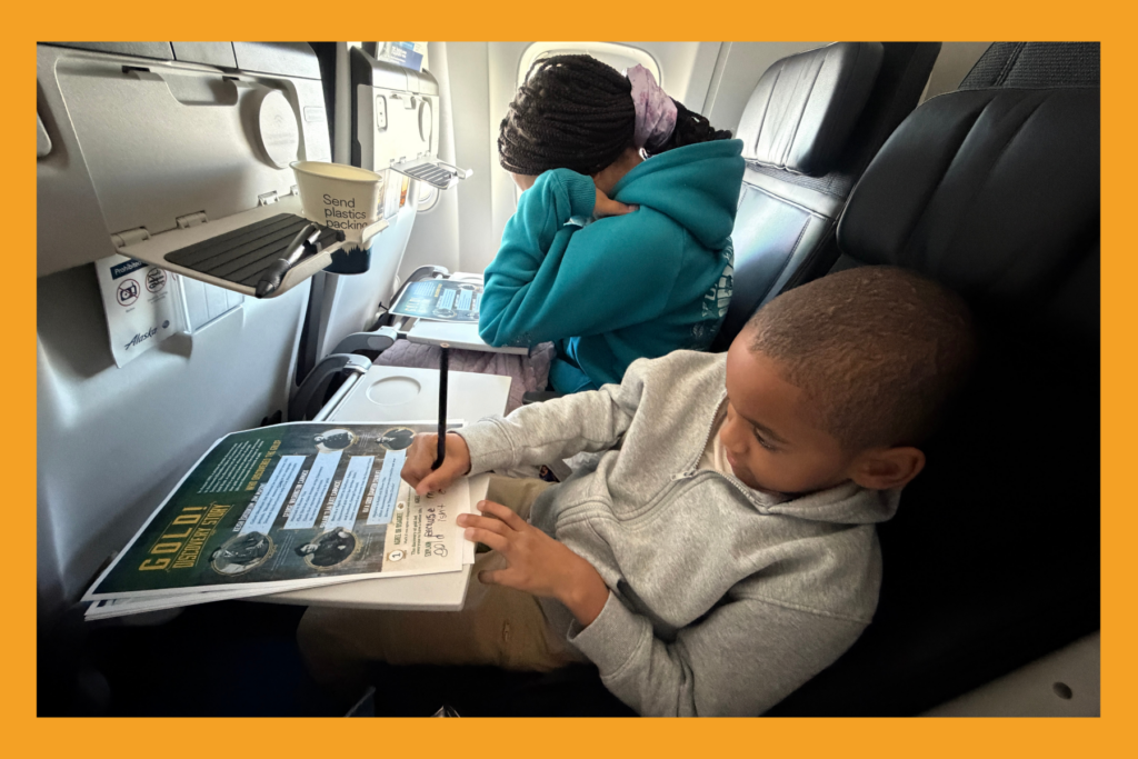 two kids on an airport completing worksheets.