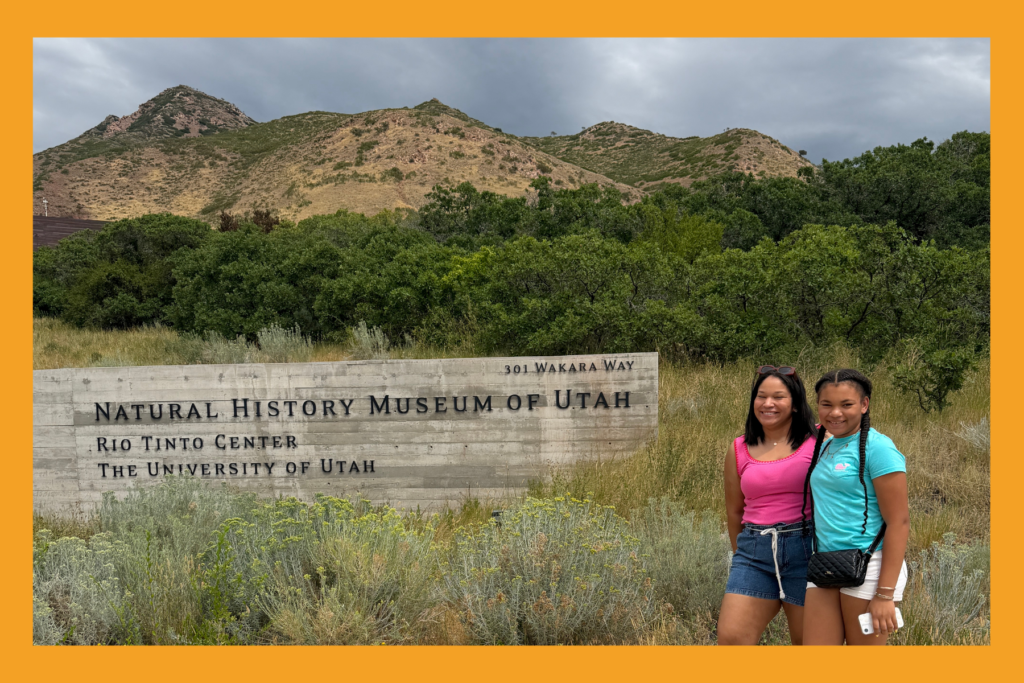 mom and daughter pose in front of the natural history museum of Utah sign.