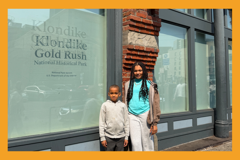 A brother and sister half smile in front of the Klondike gold rush national historic park.