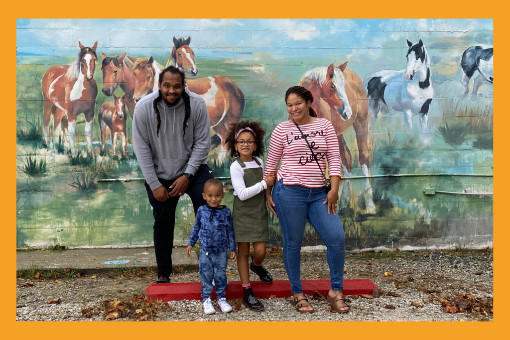 a family poses in front of a mural of horses.