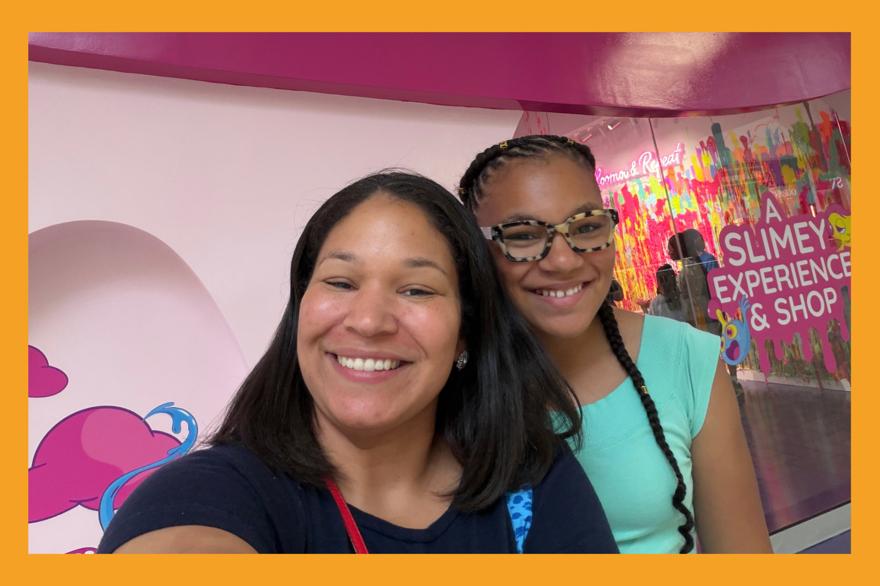 A Mom and daughter smile in front of "A Slime Experience" at Slomoo at Tysons Corner.