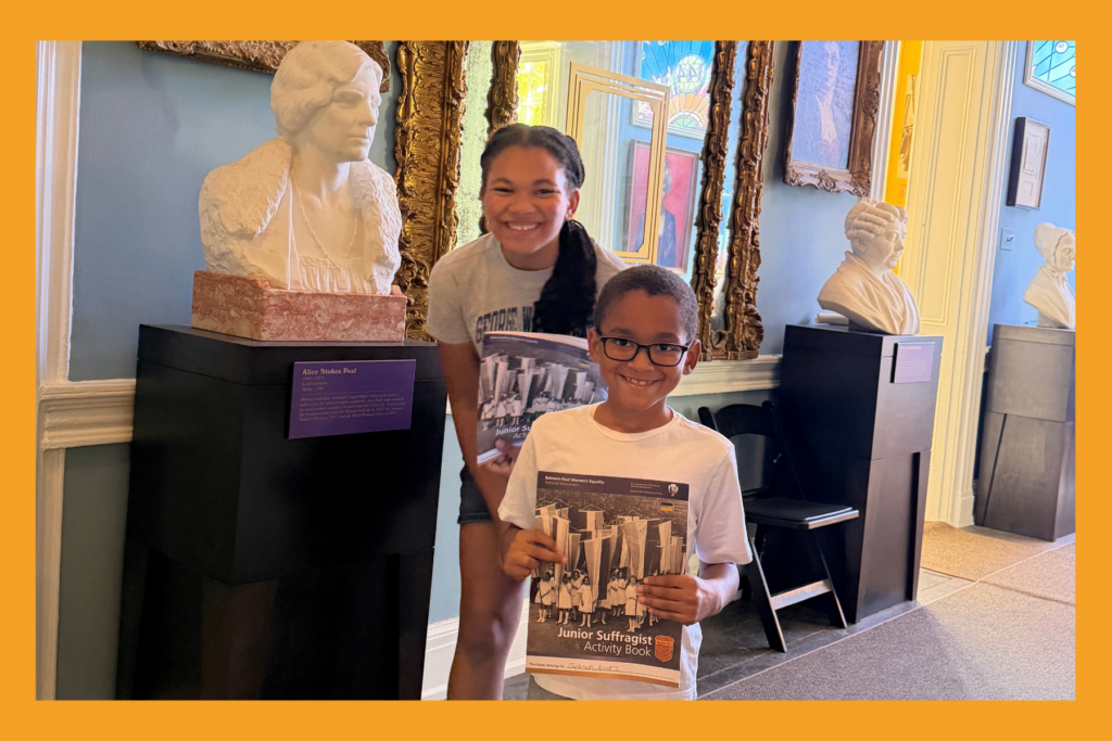 Two Children pose with a statue head of Suggragist Alice Paul holding their junior ranger activity books.