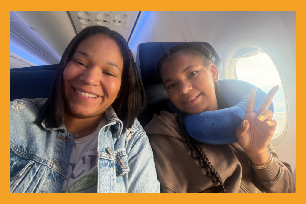 mom and daughter holding two fingers up while smiling, sitting on a plane.